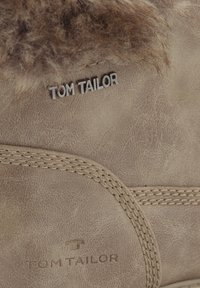Bottine en daim couleur tan avec col en fausse fourrure, coutures visibles et logo "TOM TAILOR" embossé sur le côté, surface en cuir texturée.