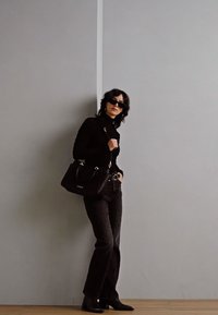 Un col roulé noir à côtes, un jean noir taille haute, des bottes à talons noires et un sac à main noir structuré. Des lunettes de soleil slim complètent le look.