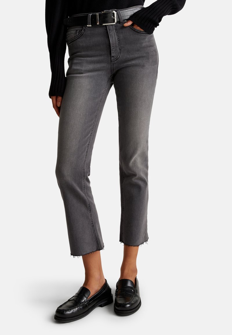 Jeans de mezclilla gris con corte recto, dobladillo deshilachado y cintura alta. Combinados con mocasines negros y un cinturón negro texturizado.