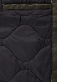Gestepptes Gewebe in Dunkelgrau mit olivgrünen Lederakzenten. Verfügt über ein wellenförmiges Nähmuster und eine Klapptasche an der Oberseite. Glatte Textur.