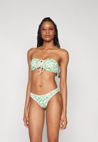 Zöld és rózsaszín bikinitartó, amely strapabíró topból áll, elöl megkötő pánttal és a hozzá illő alacsony derekú, levelekkel mintázott alsóval.