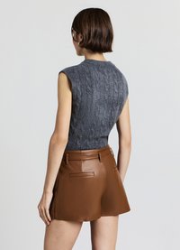 Haut sans manches gris en maille avec un motif torsadé texturé, associé à un short marron en similicuir avec poches arrière et coupe ajustée.