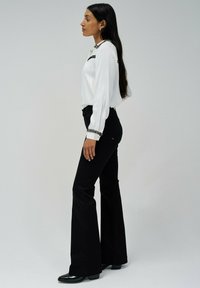 Blusa blanca de manga larga con acentos negros, combinada con pantalones de campana negros y botas brillantes negras. Tejido suave y ajuste entallado.