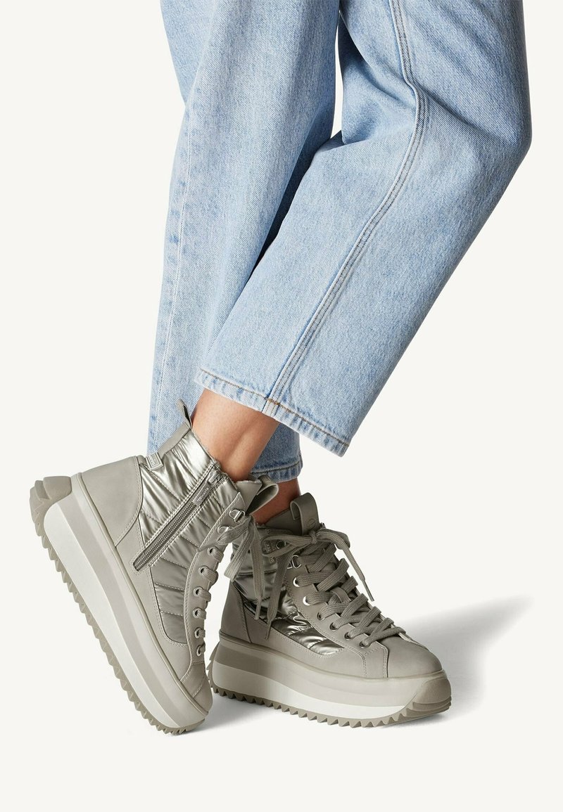 Des baskets montantes en cuir gris clair avec des accents métalliques, des côtés texturés, des semelles blanches épaisses et des lacets gris, assorties à un jean bleu clair.