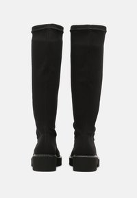 Botas negras sobre la rodilla hechas de un tejido elástico, con suela plana, detalles de costura sutiles y un diseño ajustado y suave.