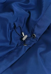 Chaqueta azul marino con tela suave y brillante, con cordón ajustable y acentos metálicos. Vista en primer plano que destaca la textura y los detalles.