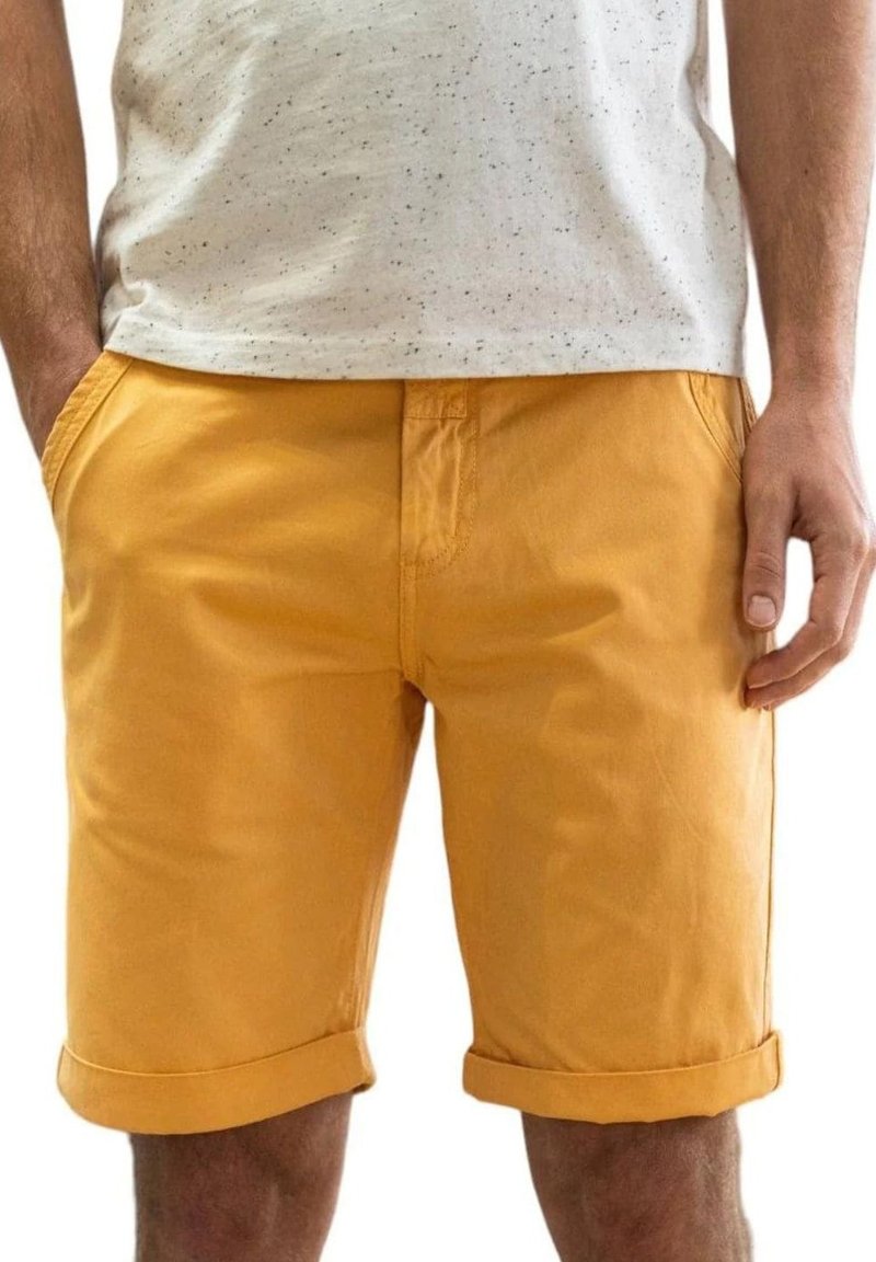 Pantalones cortos de algodón amarillos con puños enrollados, bolsillos laterales y un diseño de frente plano, combinados con una camiseta gris claro moteada.