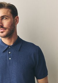 Marineblaues Strick-Poloshirt mit strukturierter Oberfläche, ausgestaltet mit einem breiten Kragen, kurzen Ärmeln und einer dreiknöpfigen Knopfleiste.
