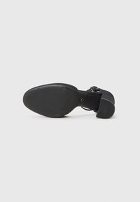 Black high-heeled sandal featuring a textured sole, a wide toe strap, and an ankle strap. The outsole exhibits horizontal grooves for traction.