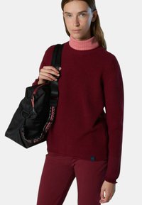 Maglione a coste bordeaux con collo alto rosa, abbinato a una borsa nera con tracolla a contrasto e dettagli in zip.