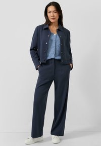 Navyblauw cropped jasje met zilveren knopen, gecombineerd met een lichtblauw gestructureerd topje en wijde navy broek. Witte sneakers maken de outfit compleet.