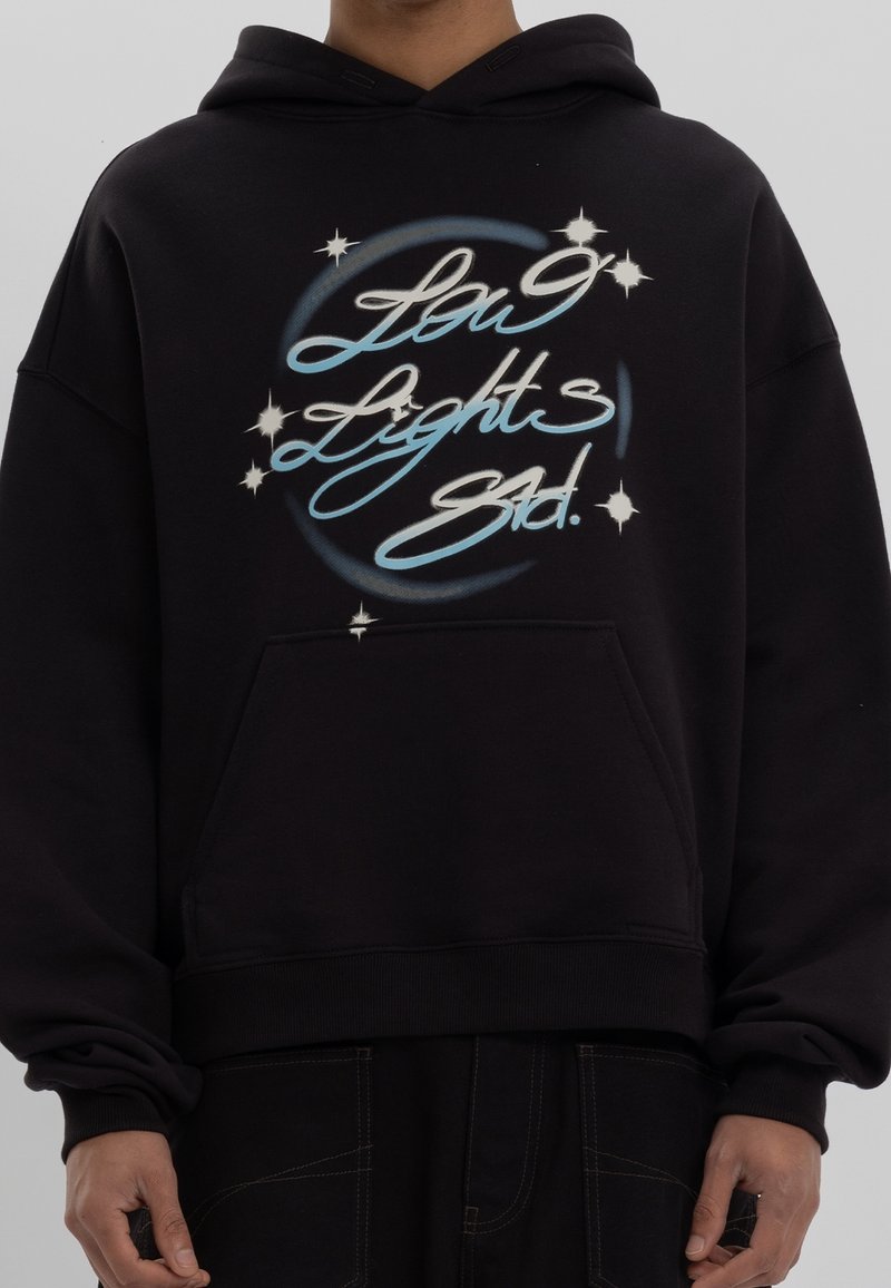 Sudadera negra oversize de algodón con un bolsillo frontal. Presenta texto gráfico en azul y blanco y acentos de estrellas en el pecho.