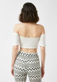 Hvid, forkortet off-shoulder top med tekstureret stof og korte pufærmer, båret med sort-hvide zigzag-mønstrede bukser med høj talje.