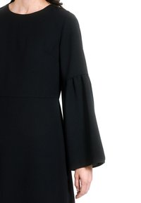 Crna haljina dugih rukava s okruglim izrezom, s gumnastim manžetama i uskim tijelom. Gladka tekstura, minimalistički dizajn, bez vidljivih uzoraka.