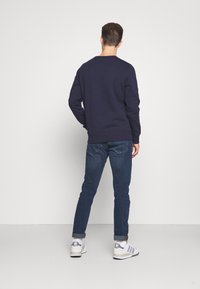 Sudadera azul marino de manga larga y cuello redondo, combinada con jeans azul ajustados y zapatillas blancas con acentos grises.