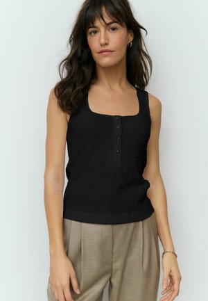 Zwart tanktop van gestructureerde stof, vierkante halslijn en vijfknopenpat. Gecombineerd met lichtbeige, geplooide broek.