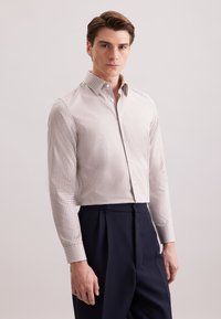 Camicia button-down bianca con un piccolo motivo a quadri rossi, maniche lunghe e un design aderente, abbinata a pantaloni blu navy a vita alta.