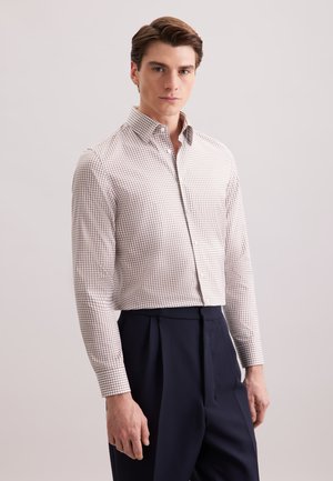 Camicia button-down bianca con un piccolo motivo a quadri rossi, maniche lunghe e un design aderente, abbinata a pantaloni blu navy a vita alta.