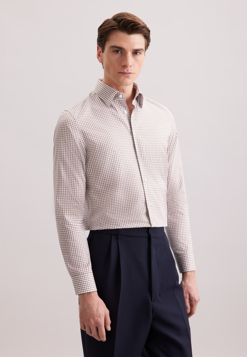 Camicia button-down bianca con un piccolo motivo a quadri rossi, maniche lunghe e un design aderente, abbinata a pantaloni blu navy a vita alta.