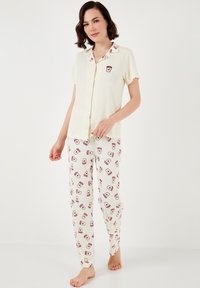 Ensemble de pyjama comprenant une chemise à manches courtes et à boutons en tissu côtelé jaune pâle, associée à un bas crème à motifs représentant des dessins de tasses rouges.
