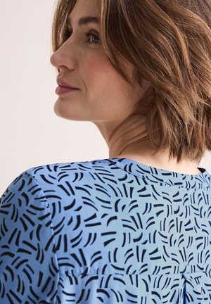 Blouse en tissu bleu avec un motif de lignes noires abstraites. Le design comprend un col rond et des manches courtes.