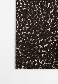 Tissu imprimé léopard noir et marron avec des taches irrégulières sur fond blanc, montrant un gros plan de l'ourlet inférieur.