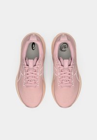 Svetlo roza športni čevlji z teksturiranim zgornjim delom iz blaga, z vezalkami in kontrastnimi belimi poudarki. Imajo oblazinjen podplat in podrobnosti z logotipom.