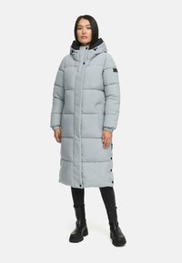 Lys grå polstret frakke med hætte, trykknapper og sidelommer. Har en quiltet design og elastiske manchetter. Bæres over sorte bukser og støvler.