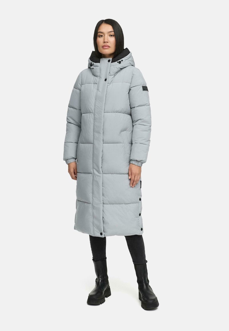 Lys grå polstret frakke med hætte, trykknapper og sidelommer. Har en quiltet design og elastiske manchetter. Bæres over sorte bukser og støvler.