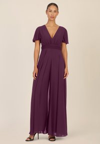 Mono de color ciruela con un escote en V profundo, mangas cortas y onduladas, y una cintura fruncida. Presenta pantalones anchos y fluidos, y una textura suave.
