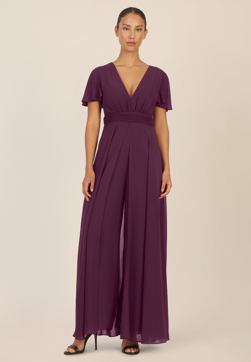 Mono de color ciruela con un escote en V profundo, mangas cortas y onduladas, y una cintura fruncida. Presenta pantalones anchos y fluidos, y una textura suave.