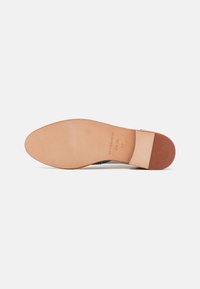Suola in pelle con una finitura liscia beige, caratterizzata da un tacco leggermente sollevato e un logo del marchio impresso. Bordo pulito e senza motivi visibili.