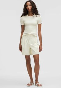 Svetlá krémová blúzka s krátkym rukávom a zodpovedajúce skladané šortky. Obe majú hladkú textúru a šortky disponujú bočnými vreckami. Súčasťou sú aj neformálne topánky.