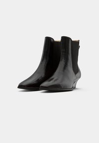 Botas pretas de tornozelo com textura de crocodilo, bico apontado e painéis laterais elásticos. O salto é baixo e ligeiramente afunilado para estabilidade.