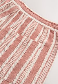 Tela a rayas rojas y blancas con un tejido texturizado. Cuenta con una cintura elástica y un bolsillo en la parte delantera, mostrando un diseño casual.