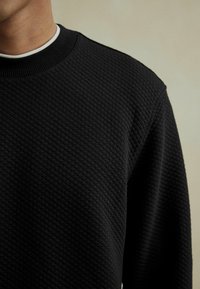 Maglione nero con texture, caratterizzato da un design trapuntato, scollatura rotonda e colletto a costine. Il tessuto sembra morbido e spesso.