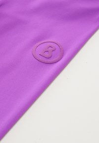 Paarse stof met een ribbelstructuur heeft een ronde reliëflogo, waarop de letter "B" binnen de cirkel staat.
