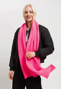Lys pink tørklæde lavet af blødt stof, med en ribbet kant. Bæres løst over en sort jakke med lynlås. Glat tekstur, livlig farve.