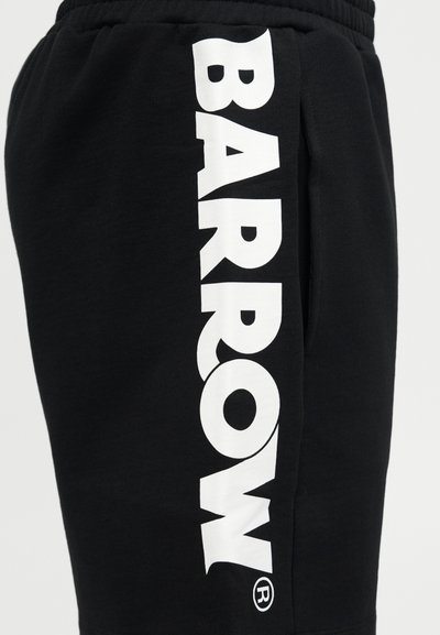 Čierne tepláky s veľkým bielym vertikálnym nápisom "BARROW" vytlačeným pozdĺž boku a elastickým pásom viditeľným na vrchu.