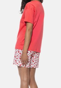 Koralle Baumwoll-T-Shirt mit kurzen Ärmeln kombiniert mit rosa Shorts mit einem Kirschmuster. Einfaches Design, weiche Textur, Freizeitbekleidung.