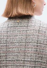 Veste en tweed présentant un motif multicolore de fils roses, noirs et blancs ; finition avec un bouton doré au niveau de l'encolure arrière.