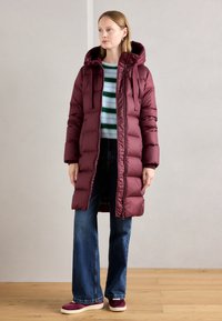 Bordeaux puffer jas met capuchon, rits en koordjes; gecombineerd met gestreepte trui en wijde jeans; gladde textuur.