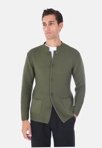 Cardigan verde oliva, con texture, dal collo rotondo, bottoni frontali e due tasche laterali. Taglio aderente, materiale a coste, senza fantasia.