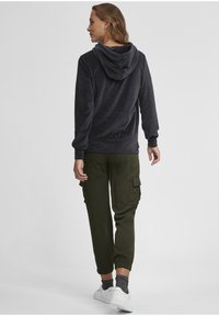 Fleecehuvtröja i mörkgrått med en huva, tillsammans med olivgröna cargobyxor med sidofickor och elastiska mudd. Vita sneakers fulländar outfiten.