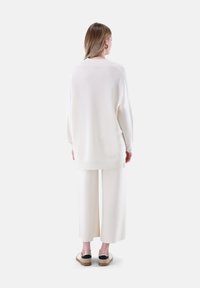 Weißer, übergroßer Pullover mit einer weichen Textur, kombiniert mit passenden weit geschnittenen Hosen. Die Schuhe haben einen schwarzen Akzent auf einem hellen Grund.