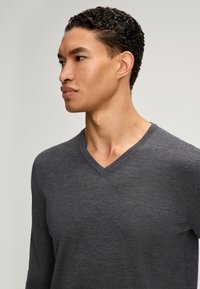 Pull à col en V gris foncé en matière tricotée douce, doté de manches longues et d'une coupe ample. Design minimaliste sans motifs ni accents visibles.