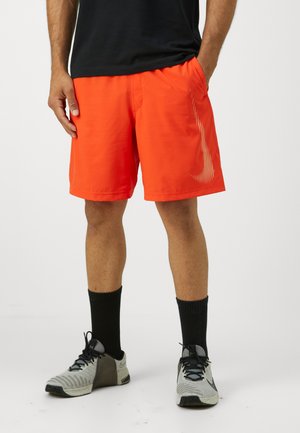 Orange atletiska shorts i ett lätt material, med sidofickor och ett vertikalt randmönster längs sidan. Bärs med svarta strumpor och skor.