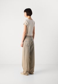 Beige avkortet T-skjorte med korte ermer, kombinert med løstsittende, lys beige denimjeans med to baklommer og subtil søm.