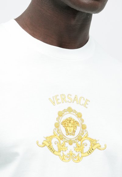 Hvid bomulds t-shirt med et gulligt Medusa-logo og et udsmykket design over teksten "VERSACE" og "SINCE 1978." Klassisk rund halsudskæring.