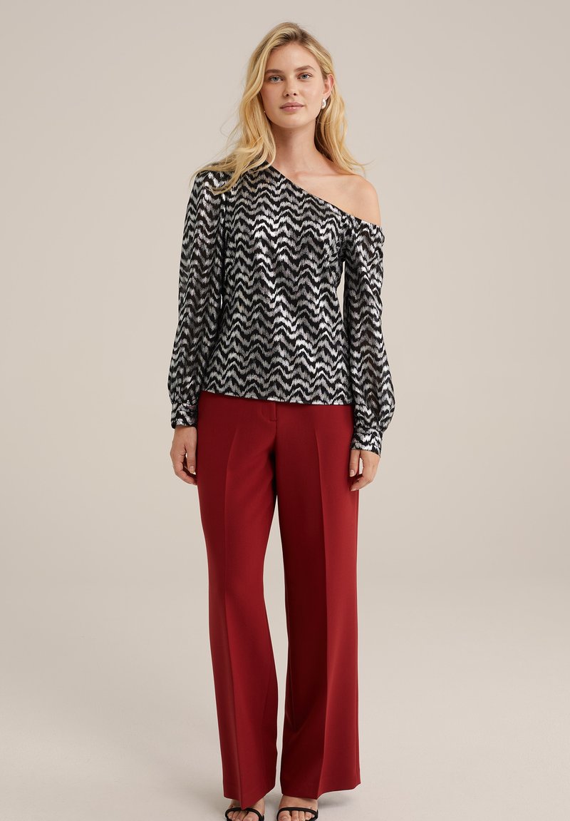 Schwarz und silber mit Zickzackmuster, schulterfreies Oberteil mit langen Ärmeln, kombiniert mit roten, weit geschnittenen Hosen. Glatte Textur, lockere Passform.